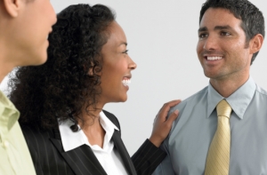 Man looks happily at another man almost out of shot with his back to the left of the camera. A woman stands between them with her hand on the happy man&#039;s shoulder.